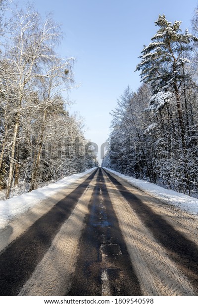 narrow snow-covered winter road for car traffic,\
Sunny day with blue sky on the road, snow on the road melts from\
car traffic