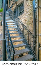 Narrow Staircase With Wrought Iron Railings Near The Stone Wall At River Walk- San Antonio, Texas. There Are Two Pole Pillars At The Bottom Of The Stairs Beside The Painted Stone Walls.