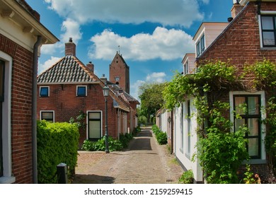 Narrow street with old houses and a church tower in the traditional Dutch village of Garnwerd, province of Groningen, the Netherlands
				