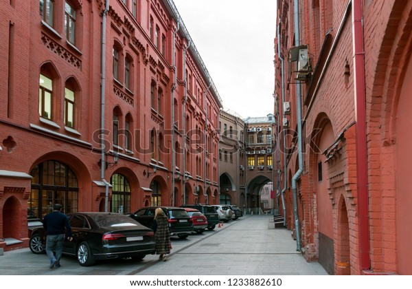Narrow street with red brick houses and parked\
cars in Moscow, Russia