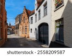 A narrow street with a row of old, historic houses in the city center of Bruges, Belgium. The houses are built in a traditional Flemish style with brick facades and gabled roofs.