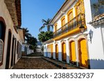Narrow street with a wonderful colonial building with yellow wooden doors, windows and balustrade in late afternoon sun, historic town Paraty, Brazil