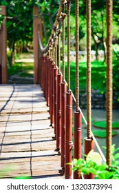 A Narrow Suspended Wooden Bridge Hangs On A Rope Above The Water.  Tropical Park In Vietnam With Green Vegetation