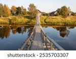 Narrow suspension bridge over the Olonka River in the village of Verkhovye, Olonetsky district, Karelia. Summer time, sunset