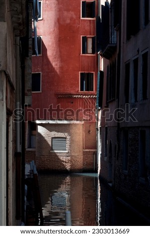 Narrow Venetian canal with red building and reflection in the water. Light and shadow