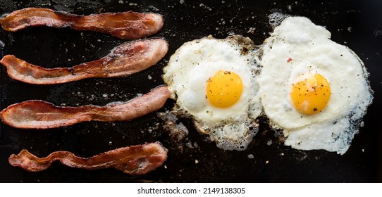 Narrow view of bacon and eggs frying on a cast iron griddle pan. - Powered by Shutterstock