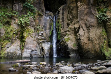 A narrow waterfall falls between rocky stone walls to a lake in the middle of a forest - Powered by Shutterstock