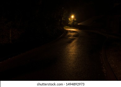 Narrow winding street in the old town with backlit sidewalks. Night shooting, the roof of the house and the street lamp after the rain.