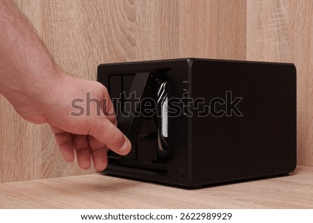 NAS server. Network storage. A man's hand opens a cell with a disk on a device for backing up data on a brown shelf. Data storage issues.