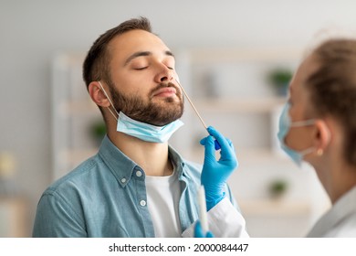 Nasal coronavirus PCR test. Doctor using swab stick to take covid virus specimen from potentially infected young guy at home. Viral disease prevention and diagnostics concept - Shutterstock ID 2000084447
