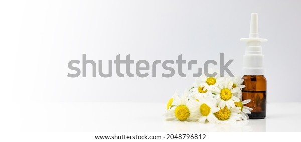 Nasal spray and natural chamomile on a white\
background. Treating seasonal allergies. Banner, side view, place\
for text.