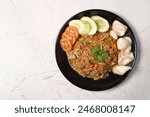 Nasi Goreng - Indonesian Chicken Fried Rice on black plate in female hands. Nasi Goreng is an Indonesian cuisine dish with jasmine rice, chicken meat, fried onion, egg and vegetables. Indoneisan Food