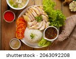 Nasi Hainan or Hainan chicken serving on wooden table with tofu soup, tomato, letuce and cucumber. Hainanese chicken rice is a dish of poached chicken and seasoned rice from Hainan, Southern China.
