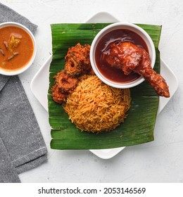 Nasi Lemak With Fried Squid And Rendang Chicken On Banana Leaf And Curry In White Background Top View