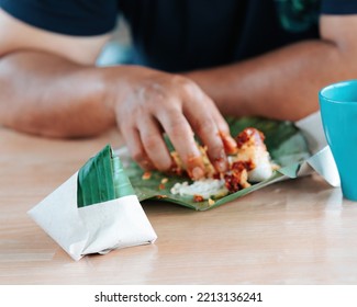 Nasi Lemak Wrapped In Banana Leaf With Brown Paper With People Eating In The Background.