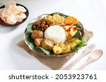 Nasi uduk is a coconut steamed rice dish from Betawi,Jakarta. Topped with several dishes and served on rattan plate. White background