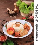 Nasi Uduk, Indonesian Food for Breakfast. Steamed Rice Cooked with Coconut Milk, Served with Fried Chicken. boiled Egg, Tempeh Oreg, and Bihun traditional concept on wooden tray
