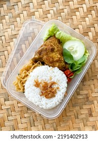 Nasi uduk or nasi lemak with fried chicken complete with noodles, vegetables such as basil, cucumber, cabbage, and chili sauce in a plastic box container. Woven Bamboo Background. Top View. - Shutterstock ID 2191402913