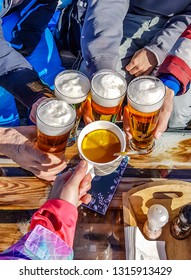 Nassfeld/ Austria - 02 23 2018: Apres Ski Drink In A Cottage, Four People Drinking Beer And One Drinks Tea With Orange. Sunny Day. Thick Foam On Each Beer, Some Spices Lie On The Table.