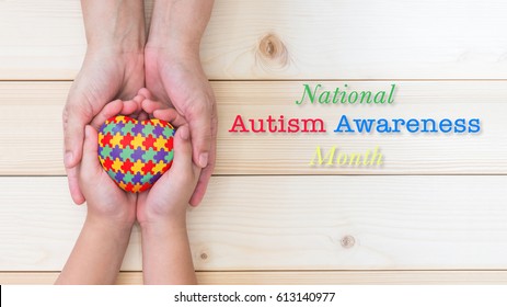 National Autism Awareness month in April with heart in puzzle jigsaw pattern on autistic kid palms supported by family caregiver hands - Powered by Shutterstock