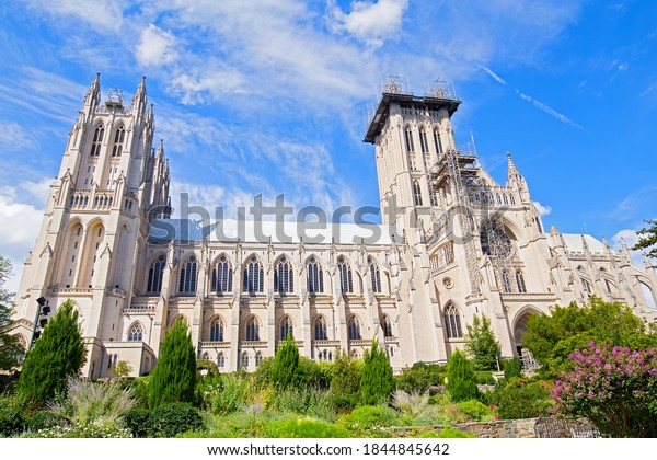 National Cathedral and gardens of Washington DC,\
USA. Gothic building surrounded by gardens under blue sky with\
cloud on a sunny day in\
spring.