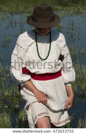 National clothes - a girl standing in a pond in a hat with a machete
