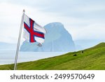 National Faroese flag waving against a background of green hills with sheeps and Koltur island, Faroe Islands, Denmark. Landscape photography