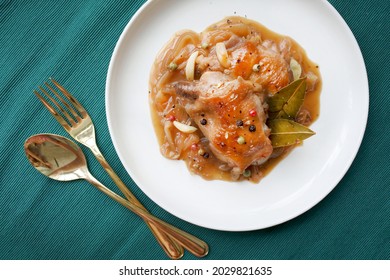 National filipino dish, Chicken Adobo, chicken thighs cooked in sauce with soy sauce, vinegar, black pepper and bay leaves. Close-up on a white plate on the table. Green napkin background. Horizontal.