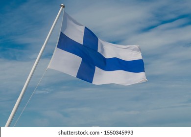 the national flag of Finland, a blue cross on a white canvas, the symbol of Finland. Finnish flag flying in the wind against the sky with clouds.