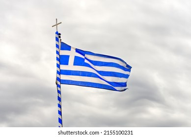 The national flag of Greece looks like 9 white and blue stripes with a cross on a background of a gray cloudy sky. close up