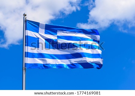 The national flag of Greece looks like 9 white and blue stripes with a cross on a background of blue sky in the summer afternoon.