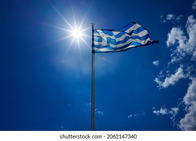The national flag of Greece is waving in the clear blue Greek sky. The white cross symbolises Eastern Orthodox Christianity, the prevailing religion of Greece.