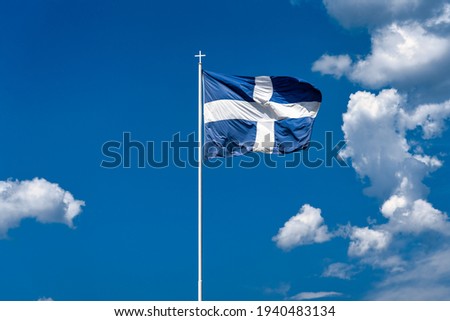 The national flag of Greece is waving in the clear blue Greek sky. The white cross symbolises Eastern Orthodox Christianity, the prevailing religion of Greece.