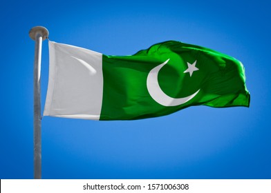 National flag of Pakistan. Known as the Flag of the Crescent and Star. Pakistani flag blowing in strong wind against a pure blue sky. Symbol of national patriotism
