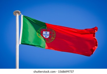 National flag of Portugal. Known as the flag of the quinas. Portuguese flag blowing in strong wind against a pure blue sky. Symbol of national patriotism