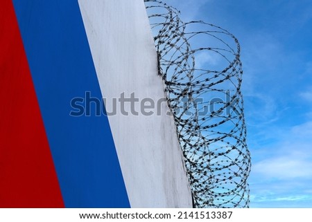national flag of Russia on concrete wall, barbed wire fence, concept of prison, symbol of police state, territory border, totalitarian regime, restriction of rights and freedoms of citizens