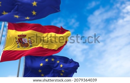The national flag of Spain waving between two European Union flags with blue sky in the background. International relations and European diplomacy.