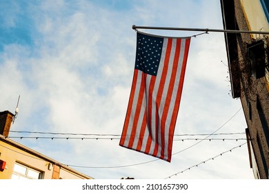 National Flag Of United States Of America Hanging In A Small Town, Blue Sky Background. Patriotic Feeling Towards USA Concept