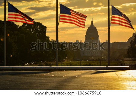 National flags and United States Capitol Building in a dramatic cloudy sunrise - Washington D.C. United States of America
