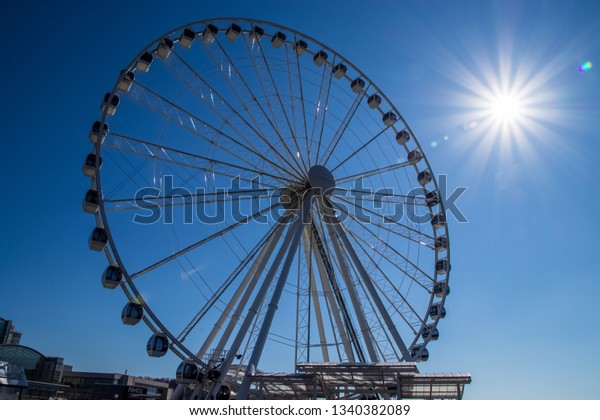 National Harbor,\
MD / United States - 3/13/19: Sunbeams extend over a ferris wheel\
on the pier at National Harbor,\
MD