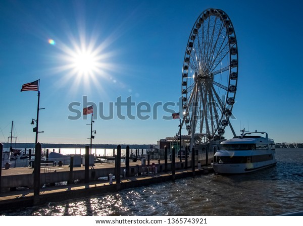 National Harbor, MD / United States - 3/12/19:
Bright sunbeams over National Harbor's pier with American Flags
flying and boat marina