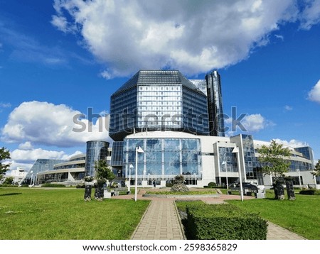 National Library of Belarus in Minsk, a modern glass building with lush lawns and flowerbeds, under a bright blue sky
