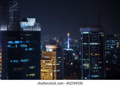 National Monument Of Indonesia In The Middle Of The City Light And Between The High Rise Building In The Night. 