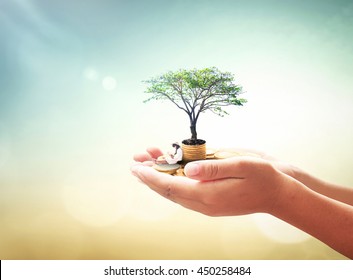 National Philanthropy Day Concept: Human Hand Holding A Girl Reading Book, Stack Of Golden Coins And Big Tree On Blurred Autumn Sunset Background