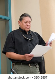 Native American Man Stepping Out Of An Office Building And Reading Papers.