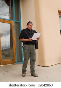 Native American Man Stepping Out Of An Office Building And Reading Papers.