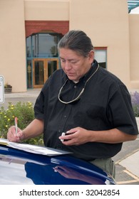 Native American Man Writing Notes On The Hood Of His Car.