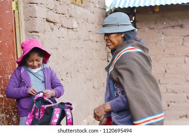 Native American Old Woman Wearing Typical Aymara Clothes And Her Little Granddaughter Holding Pink Backpack.