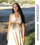 Native American woman standing with long black hair and wearing a white embroidered dress.