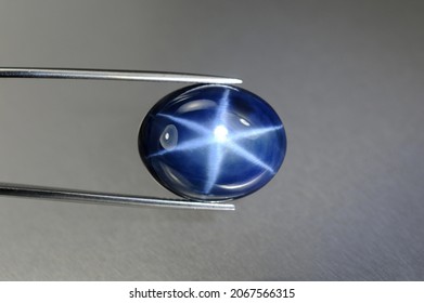 Natural 6 rays blue star sapphire gemstone in tweezers. Heated, diffusion treated, opaque, oval cabochon polished loose setting for making jewelry. Natural mined genuine corundum. Gemology, mineralogy - Shutterstock ID 2067566315
